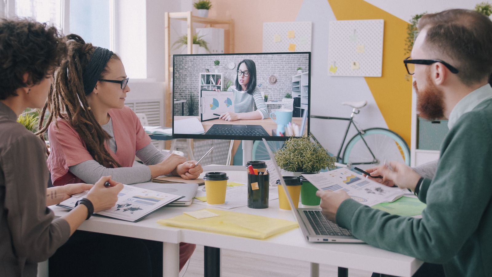 A team in the office joined by a colleague on a large screen
