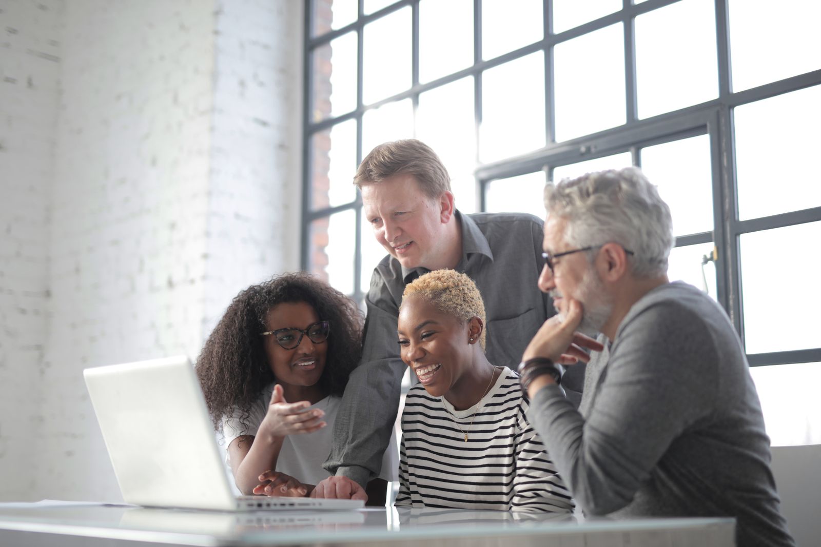 A small team gathered around a laptop by a bright window